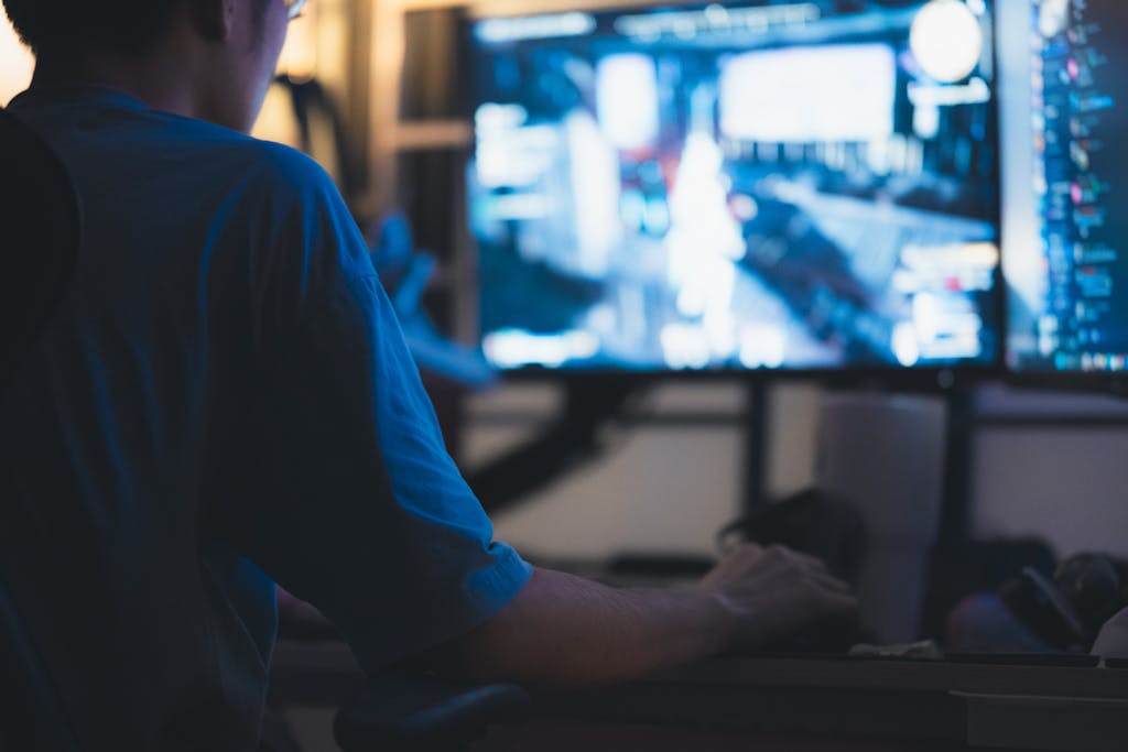 A man intensely focused on a computer screen in a dimly lit room, showcasing concentration in technology.